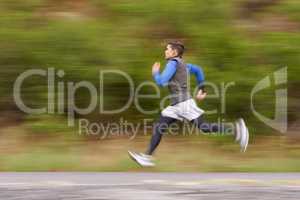 Burning away the miles. Motion blurred image of a young man running along the road.