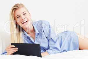 Connect anywhere, any time. A beautiful young blonde woman lying in bed with her digital tablet.