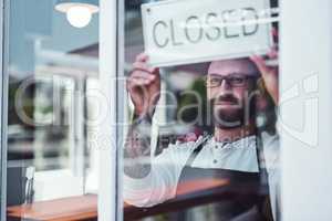 Business is over for the day. Cropped shot of a handsome young barber hanging up a closed sign on the window of his barbershop.