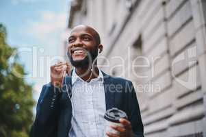 Im listening to my favourite motivational speaker. Shot of a businessman holding a coffee and listening to music through earphones while walking through the city.