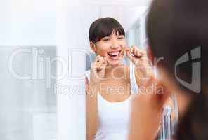 Flossing away. Shot of a cheerful attractive young woman flossing her teeth while looking at her reflexion in a mirror at home.