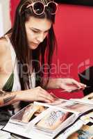 Finding the right design to add to her collection. Shot of a beautiful young tattooed woman paging through an album of tattoo designs.