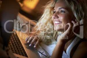 Nocturnal socializing online. Shot of a young woman using her laptop on her bed at night.