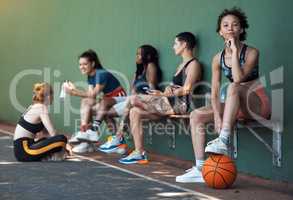 Think youve got what it takes. Full length portrait of an attractive young female athlete sitting on a bench at the basketball court with her teammates in the background.