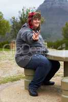 Peace out. An obese young man sitting outside at a picnic table showing a peace-sign.