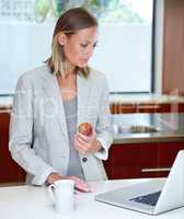 Ready for the day ahead. A young woman standing by the kitchen counter with her laptop and a light breakfast.