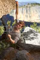 Courageous climber. Portrait of a rock climber dangling from one hand off the edge of a cliff with view of mountains in the background.