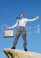 Theres no limit to what I can achieve now. An elated young businessman holding a briefcase standing atop a cliff.