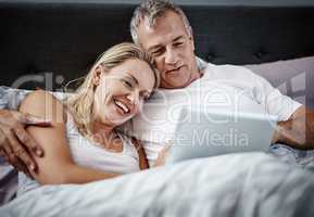 Staying in and unwinding. Shot of a mature couple using a digital tablet while lying in bed.