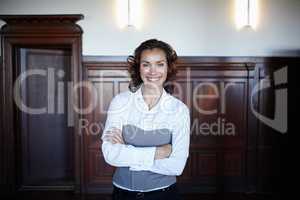 Shes a positive influence in the courtroom. Cropped shot of an attractive female laywer standing with her arms folded and smiling widely in the courtroom.