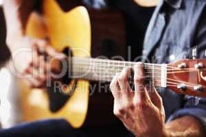 His skill has been gained through hours of practice. Cropped view of masculine hands strumming a guitar.