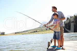 Steady now. Shot of a father and son fishing on a dock.