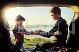 Thats what big brothers are for. Shot of a young surfer helping his little brother put on his wetsuit at the beach.