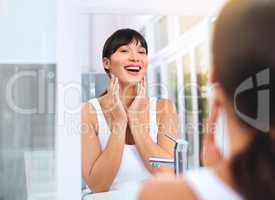 Shes glowing today. Shot of a cheerful attractive young woman applying moisturizer on her face while looking into her reflexion in the mirror.