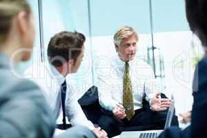 Business man conversing in meeting. Mature business man conversing with his executives during meeting.
