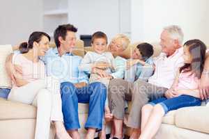 Three generations gather happily together. Three generations of family sitting together affectionately on the lounge couch.