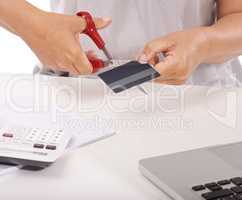 Your purchases are too extensive. Close up of a woman cutting up her credit card with a laptop and calculator in front of her.