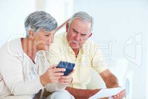 Couple calculating domestic budget. Mature Caucasian couple calculating domestic budget while sitting on couch.