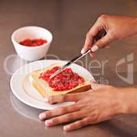 Fruity treat for breakfast. Cropped shot of a woman spreading fruity jam onto toast.