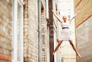 Im flying. A beautiful young woman posing playfully on a fire escape ladder in between buildings.