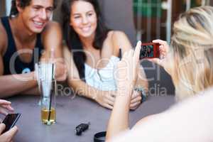 Capturing their happiest memories. Group of teens enjoying beverages while at an outdoor restaurant while taking a photo with a mobile phone.