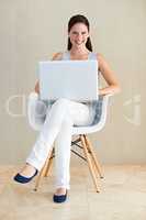 Working from the comfort of home. A pretty young woman sitting in a chair and using her laptop.
