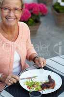 Meat fresh off the BBQ. A senior woman enjoying a delicious meal outdoors in the evening.