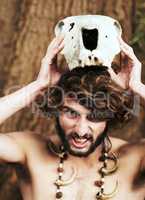 Crowning himself King of the Jungle. An aggressive caveman placing an animal skull on his head.