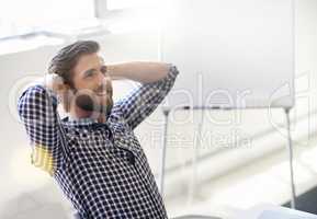 Thinking of his countless successes. Shot of handsome young man relaxing with his hands behind his head in an office.