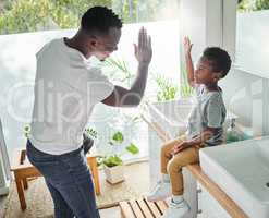 Encourage your child to follow good hygiene practices. High angle shot of a father giving his son a high five in a bathroom at home.