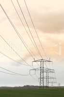 Power supply. Electricity cables running over a field against a cloudy sky.