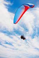 Two in one. Low angle view of two people doing tandem paragliding high up.