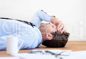 Burned out businessman - overworked. A businessman lying on the floor with hand rested on his head and paperwork lying on the floor in front of him.