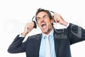 Business man shocked by loud music on headphones. Shocked mature business man removing headphones against white background.