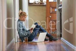 Jotting down some private thoughts. A young woman sitting on the floor doing some researching on her laptop.