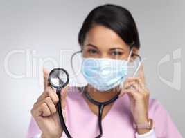 Youve got a strong heart. Cropped portrait of an attractive young female healthcare worker wearing a mask and holding up a stethoscope in studio against a grey background.