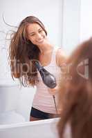 Taking care of her luscious mane. A young woman blow drying her hair in front of a mirror.