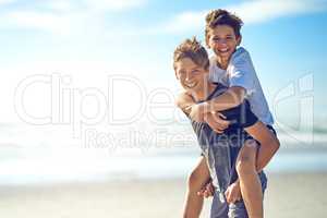 Who needs a superhero when you have a big brother. Portrait of a happy young boy giving his little brother a piggyback ride on the beach.