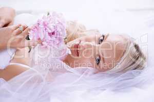 Honeymoon bliss. Closeup portrait of a gorgeous young bride lying on her bed with her bouquet.