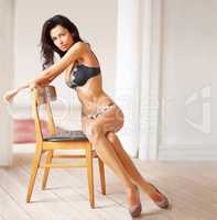 Seductive pose. Portrait of sensual brunette sitting on a chair wearing lingerie and heels.