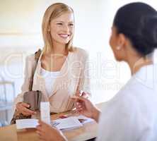 Could you put that on my card please. Shot of a young woman checking in at the reception desk.