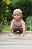 Babys first crawl. A baby crawling along a wooden surface in a garden.