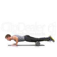 Improving his strength and flexibility. A young man doing push-ups on his exercise mat with his legs raised by a foam roller.