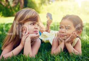 Childhood friendship. Shot of two adorable little girls lying next to each other on the grass.