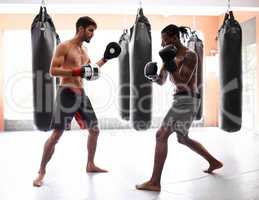Hold nothing back. Shot of a two young men practicing kickboxing in a gym.