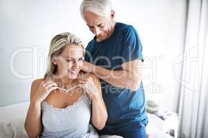 You know just how to spoil me. Shot of a mature man putting a necklace around his wifes neck at home.