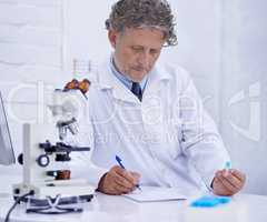 Recording his findings. A mature scientist recording observations on a piece of paper while sitting in his lab.