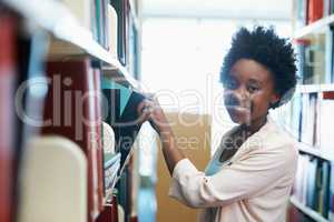 Studying for my final exam. A young woman selecting some books in the library.
