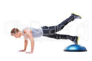 Hes working towards a toned body. A young man working his upper body using a bosu-ball.