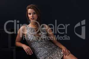 Lighting up the room with a look. Portrait of a beautiful young woman in a sequined dress posing against a dark background.